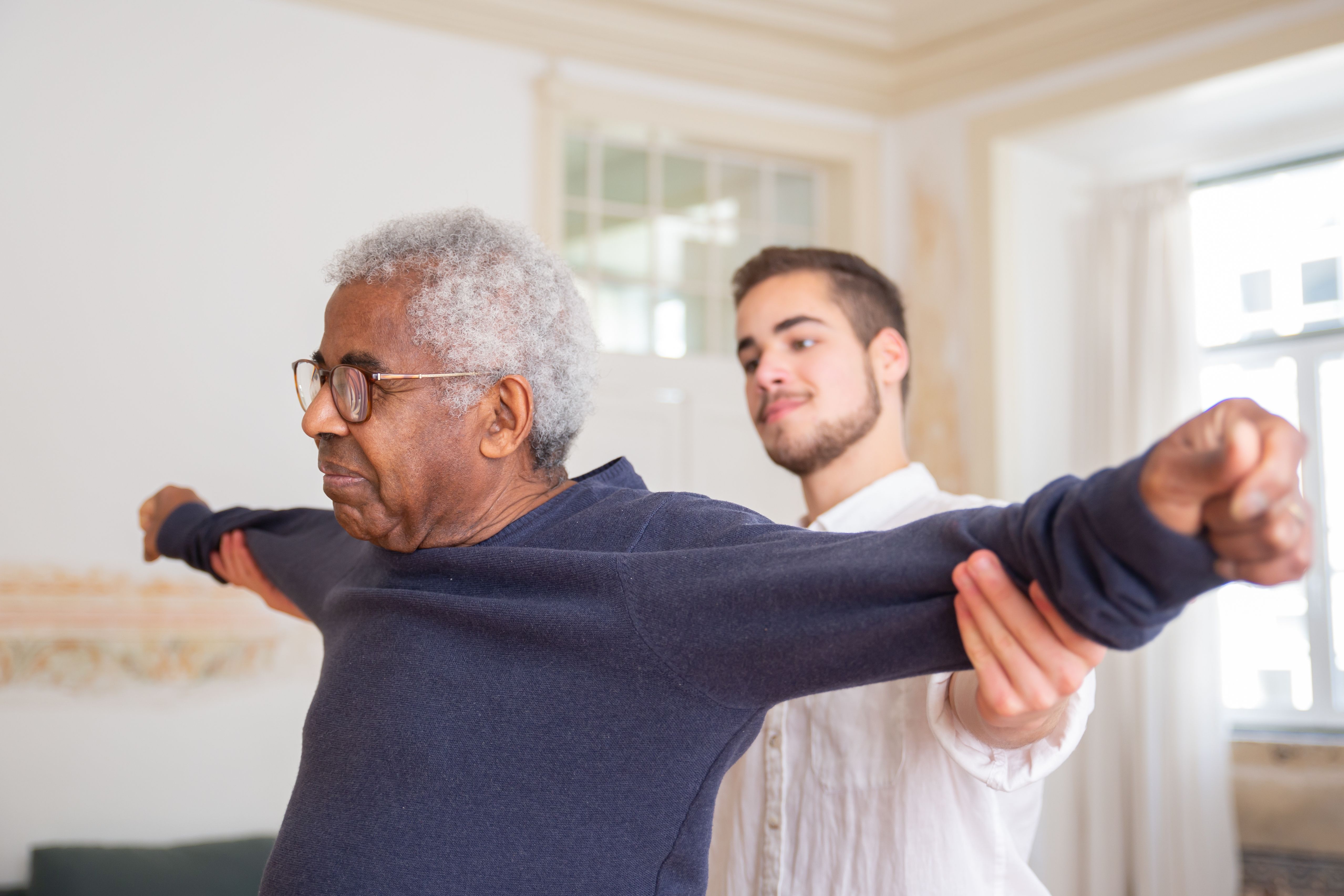 Physiotherapist guiding an elderly client through a shoulder exercise at home